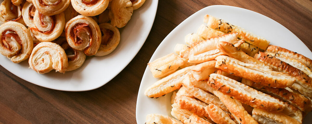 Two plates of savory puff pastry snacks on a wooden table.