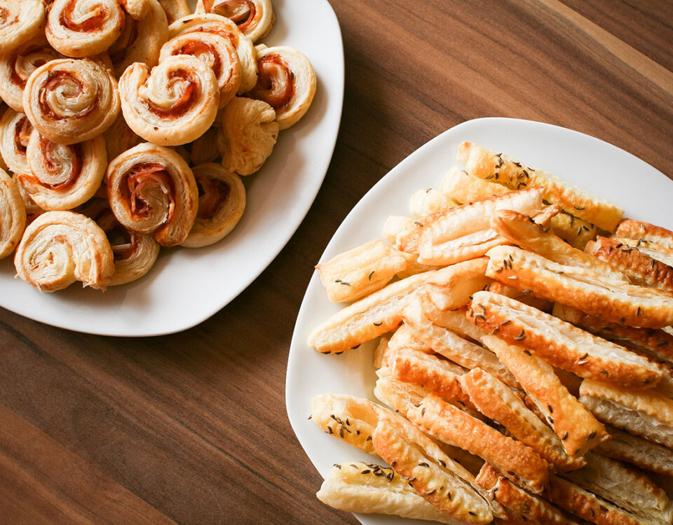 Two plates of savory puff pastry snacks on a wooden table.