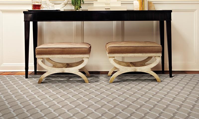 Two beige cushioned stools under a black console table on a patterned carpet.